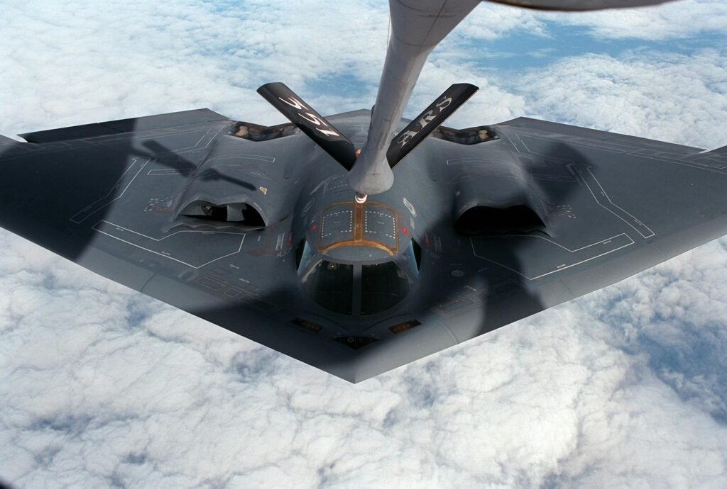 A stealth bomber aircraft receives aerial refueling mid-flight over clouds.